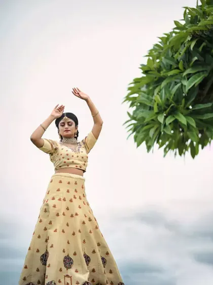 A wide shot showing the cream lehenga in a beautiful natural landscape, perfect for a pre-wedding photoshoot.