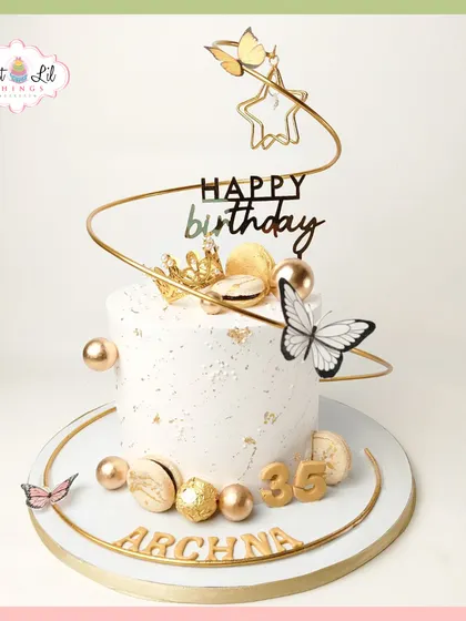 Golden glam for a 35th birthday queen. This white and gold cake is adorned with a spiral topper, butterflies, macarons, and Ferrero Rocher chocolates for a truly luxurious feel.