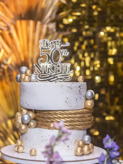 A close-up of the modern 50th birthday cake, showing the speckled finish and the contrast between the white tiers and the gold rope detailing.