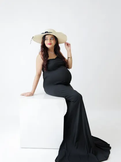 A stylish and classic portrait. The mom-to-be wears a simple black dress and a sun hat, her pose exuding confidence and elegance.
