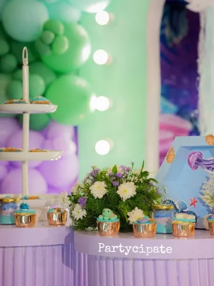 The dessert table at Viransh's party, with cupcakes and treats displayed in front of a backdrop of green and purple balloons, mimicking the colors of a coral reef.