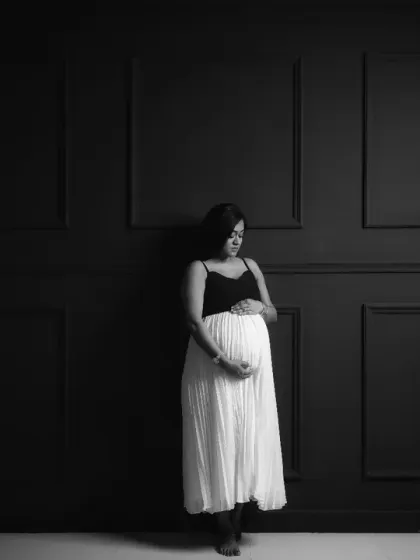 A minimalist and modern black and white portrait. The mom-to-be stands against a dark, paneled wall, creating a striking contrast that is both simple and profound.