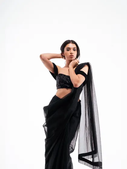 A graceful and elegant pose in a studio. The model's posture highlights the off-shoulder design of the blouse and the drape of the saree, creating a timeless fashion portrait.