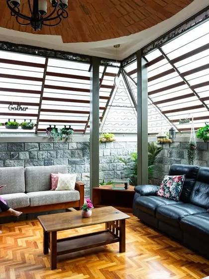 We dissolve the boundaries between inside and out. This living area uses expansive slatted windows and a stone accent wall to create a serene space that feels like a sheltered extension of the garden, filled with natural light and air.