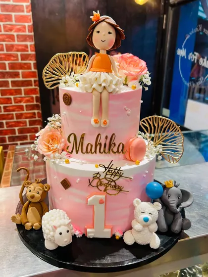 A two-tier first birthday cake with a doll topper and an assortment of cute fondant animals.