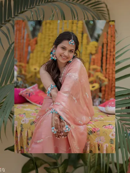 A beautiful portrait of the bride seated, framed by palm leaves, showcasing her floral jewelry.