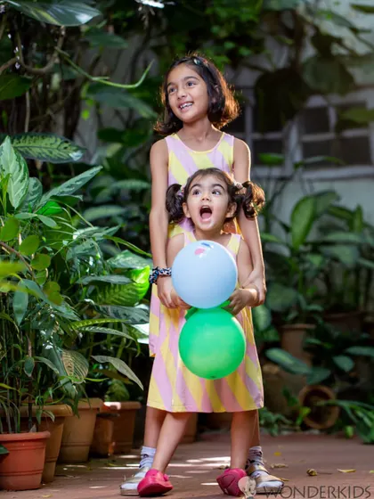 Two sisters having fun with balloons in a garden. The spontaneous joy and playful energy in this shot make it a wonderful and authentic sibling portrait.