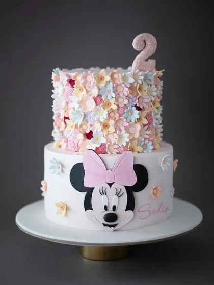 A beautiful two-tiered Minnie Mouse cake with a top tier covered in delicate pastel flowers. This is a wonderfully artistic take on a classic character theme.