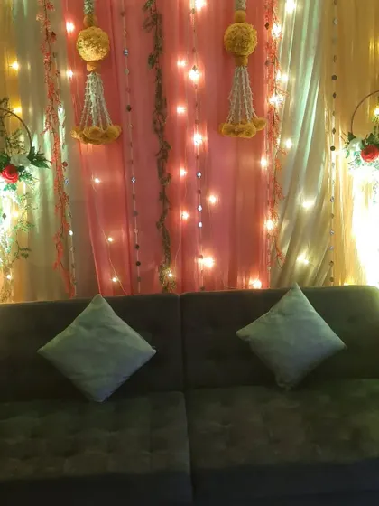 A cozy home decor setup with a sofa placed against a backdrop of shimmering drapes and traditional hangings.