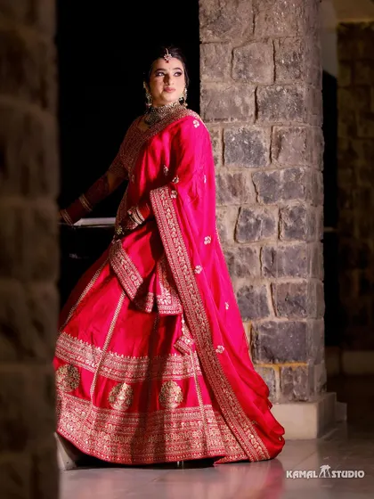 A stunning portrait of the bride in her pink lehenga, posing against a stone pillar.