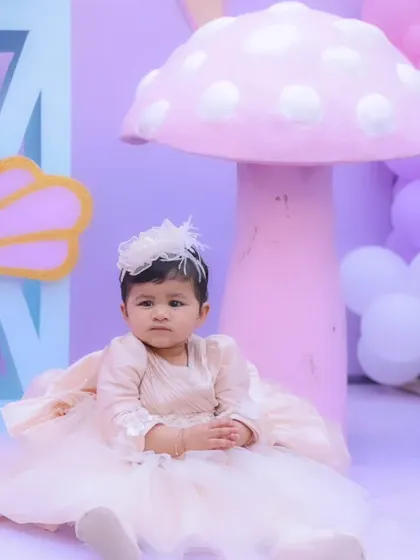 The adorable birthday girl in her pastel dress, posing in front of a giant pink mushroom prop from her butterfly wonderland.