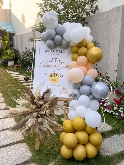 A warm welcome to an outdoor 31st birthday party. The entrance featured a custom sign on an easel, decorated with a beautiful balloon garland in mustard, grey, and peach tones, setting a stylish and inviting mood.