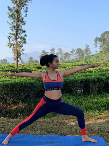 Warrior II pose amidst the vibrant green of a tea plantation. Hip openers like this increase flexibility, improve posture, and help release stored stress and emotion.