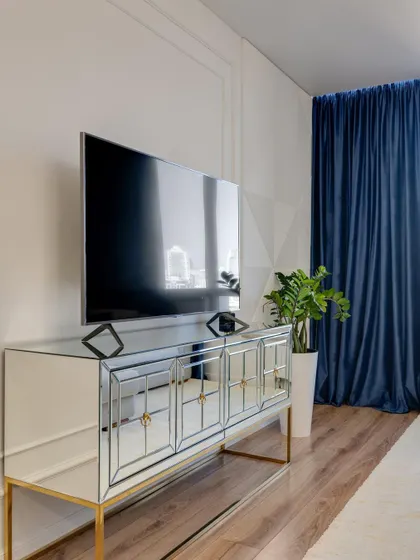 A luxurious mirrored TV console with gold-finished legs. This glamorous piece reflects light and adds a sense of space and opulence to the living room.