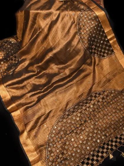 A rich brown linen saree with intricate mirror work. This piece combines the rustic charm of linen with a touch of festive sparkle.