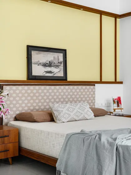 The 'Poorna' guest bedroom has a vintage, earthy feel, with a unique yellow accent wall and crisscrossing wooden ledges behind the bed.