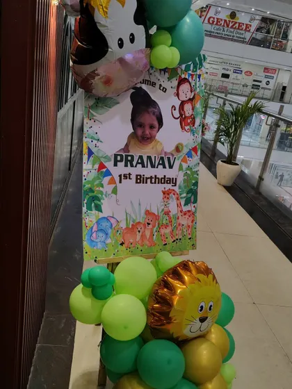 For a first birthday, a personalized welcome stand is a great touch. This jungle-themed standee features the birthday boy's photo and name, framed by a small balloon arrangement with lion and monkey foil balloons.