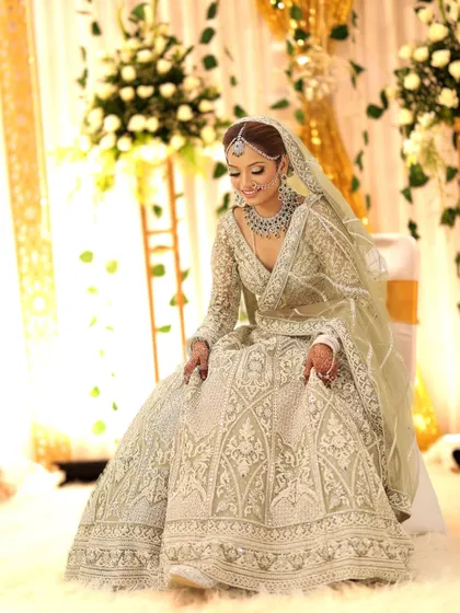 A full-length shot of the bride seated, showcasing the beautiful drape of her lehenga and the elegance of the full diamond jewellery set.