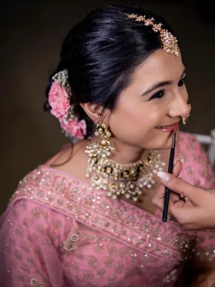 A behind-the-scenes moment, adding the final touches to this bride's simple and elegant phera look. The focus was on clean skin and soft pink tones.