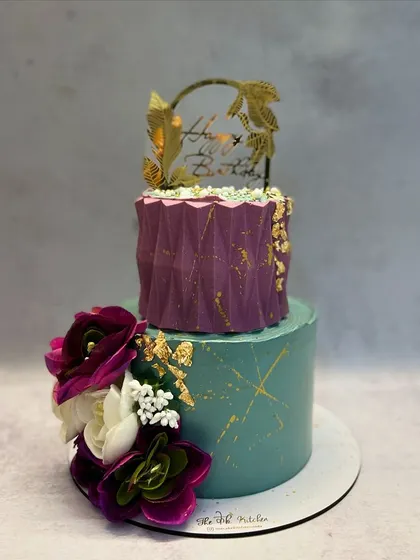 Another view of the teal and purple two-tiered cake, showcasing the beautiful arrangement of handmade sugar flowers.