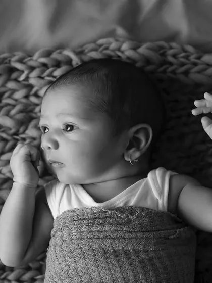 A thoughtful moment captured in black and white. This baby is lying on a chunky knit blanket, looking off to the side with a curious expression.