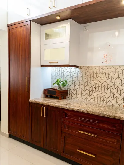 A view of the kitchen showing the tall pantry unit and custom cabinetry in a rich wood finish, contrasted with glossy white overheads. The design balances traditional warmth with modern sleekness.