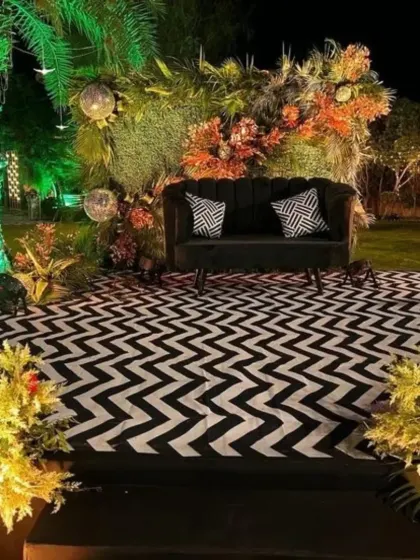 A modern and chic stage for a cocktail party, featuring a black sofa, a lush green backdrop, and a bold black-and-white chevron floor.