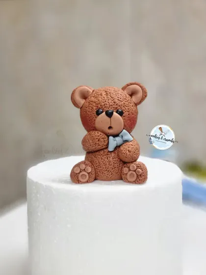 A close-up of the sweet little fondant teddy bear topper for the baby shower cake, complete with a tiny blue bow.