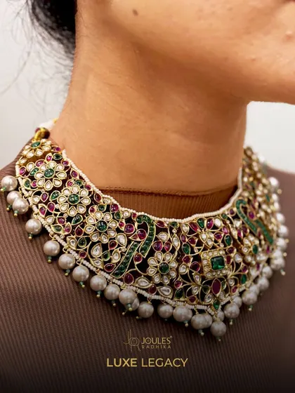 Some necklaces do not need a spotlight; they become one. This intricately detailed floral polki choker, set with rubies, emeralds, and pearls, is a masterpiece of craftsmanship.