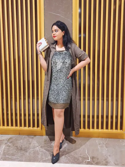 A sequined dress layered with a long, earthy-toned shrug creates a glamorous yet relaxed evening look.