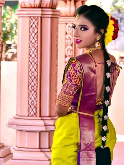 A profile view showcasing the elegant braided hairstyle adorned with flowers, which perfectly complements the colorful saree and bold makeup. This is a complete look, ideal for a pre-wedding or cultural photoshoot.