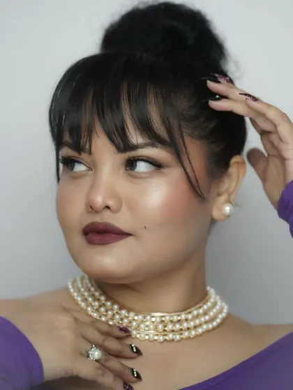 A retro-inspired look with bangs, a high bun, and a bold berry lip. The pearl choker adds a touch of classic elegance, showing how accessories can elevate your makeup.