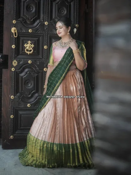 This peach and green half saree has a lovely shimmer, perfect for evening events. The model is posed against a traditional door, highlighting the outfit's classic appeal.