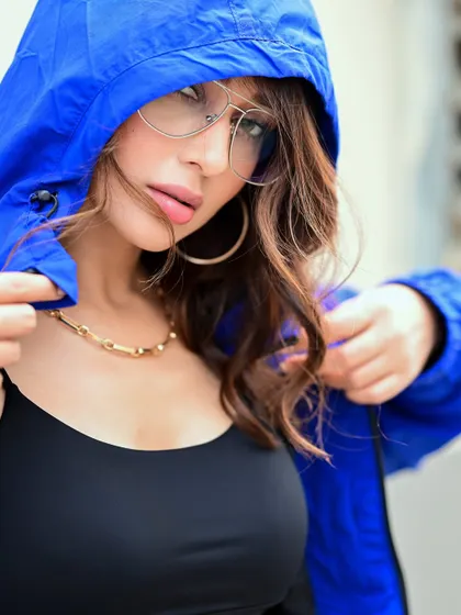 A close-up of Mimi in a hooded jacket. The composition draws attention to her face and the cool, oversized glasses, creating an edgy and fashionable look.