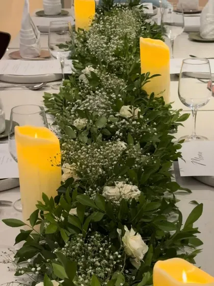 This view along the center of the table shows the full length of the greenery runner. The mix of dense foliage, delicate baby's breath, and scattered white roses creates a fresh and organic feel for the dining experience.