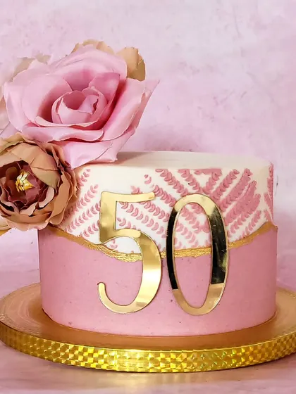 A stunning and modern cake for a 50th birthday. The design features a pink stencil pattern, a gold fault line, and is topped with beautiful sugar flowers.