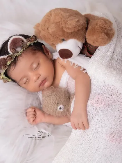 A sweet princess snuggled up with her teddy bears. The soft white blanket and the baby's deer-themed headband add a touch of woodland magic.