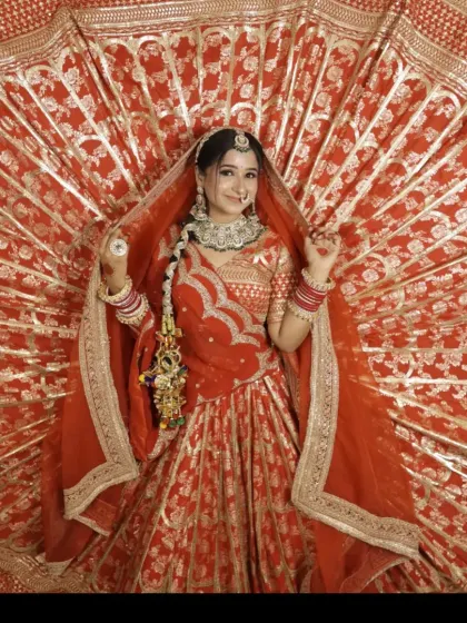 A full view of the orange-red banarasi lehenga with its skirt fanned out to show the rich fabric and gold patterns.