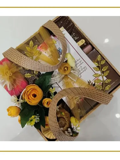 The full view of the birthday hamper in a basket with woven handles, filled with yellow flowers and golden-wrapped gifts.
