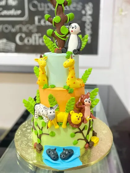A grand three-tiered jungle adventure cake. Each tier represents a different part of the jungle, with animals like hippos, monkeys, lions, and a panda.