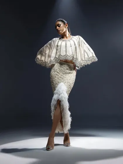 An ivory ensemble featuring a cape-style top and a fitted skirt with feather details. This look is the definition of modern couture, ideal for a bride who wants a fashion-forward look for her reception.