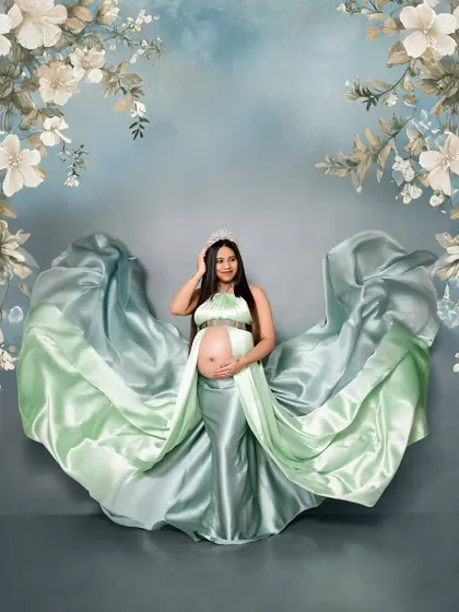 This solo portrait features a beautiful two-tone satin gown in mint green. The fabric is tossed to create a wing-like effect against a soft blue floral backdrop.