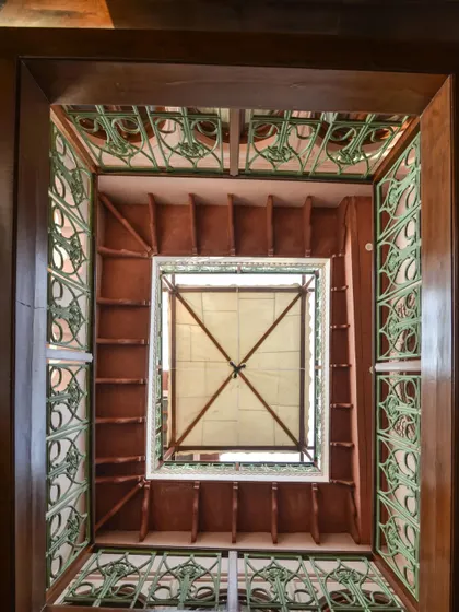 A view looking up through a smaller courtyard, showcasing the intricate design of the railings and the flow of natural light from the skylight. This detail is part of the building's passive ventilation and lighting strategy.
