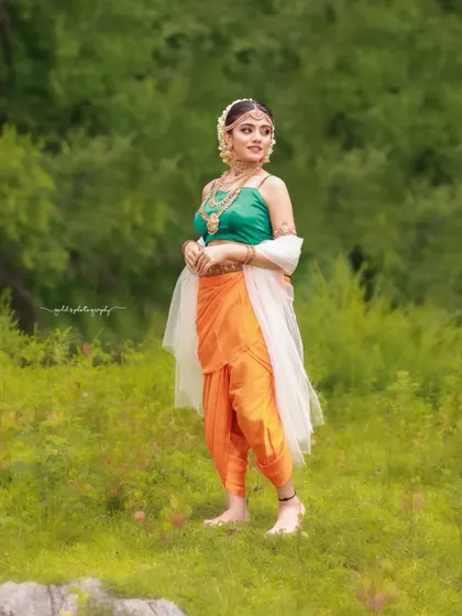 Inspired by the grandeur of Bahubali, this "Sakhi" look features a model in a unique orange and green dhoti-style saree. The outdoor setting and regal jewelry complete the ancient princess aesthetic.