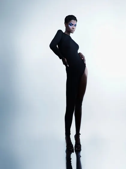 A full-length shot that plays with perception. The mirror on the floor creates a perfect reflection, making the model appear incredibly tall and statuesque.