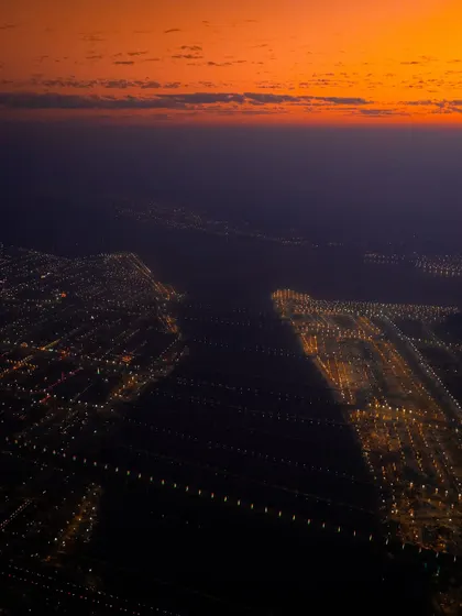 An abstract aerial photograph of Prayagraj during the Mahakumbh Mela at night. The city lights stretch across the landscape, hinting at the massive scale of the world's largest religious gathering.