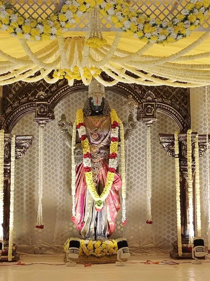 This angle highlights the intricate ceiling of the mandap, covered in yellow fabric and a web of fresh flower garlands. The stage is lit with spotlights to focus on the ceremony area.