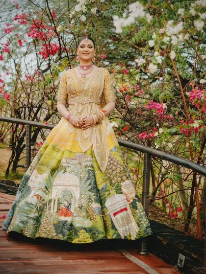 The bride poses on a wooden bridge surrounded by blooming bougainvillea. Her artistic lehenga complements the natural floral setting, highlighting a cohesive and picturesque wedding aesthetic.