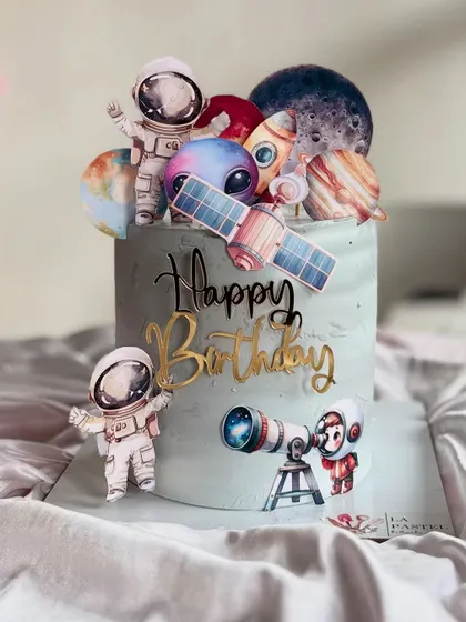 An out-of-this-world space-themed cake for an aspiring astronaut. It's decorated with planets, rockets, satellites, and little astronauts, all set against a cool grey-blue galaxy frosting.