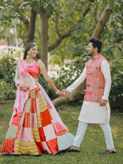 A romantic walk in the park. The couple holds hands, their colorful Haldi outfits standing out beautifully against the green surroundings.
